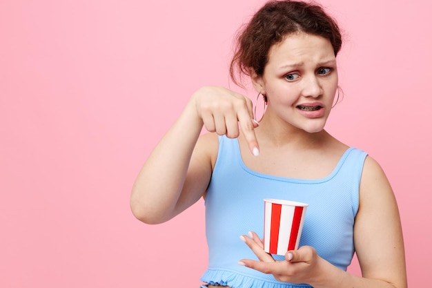 Chica hace muecas con un vaso desechable divertido fondo rosa inalterado