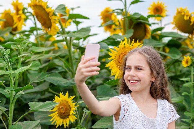 Chica hace selfie en un teléfono inteligente con una sonrisa en su rostro, contra un campo de girasoles.