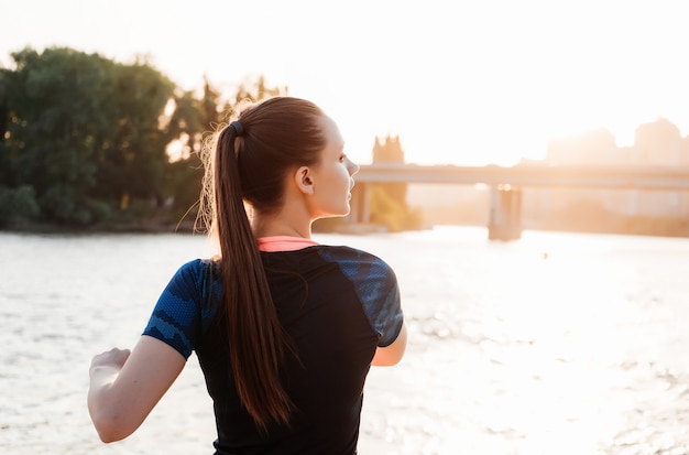 Chica haciendo calentamiento cerca de la orilla del río al atardecer