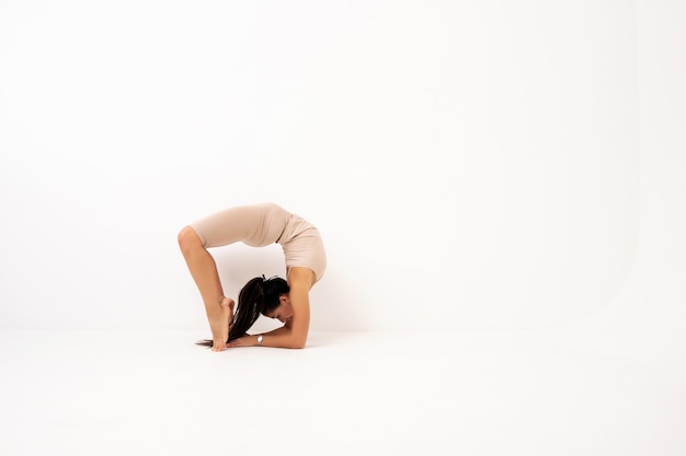 Chica haciendo estiramientos en el estudio sobre un fondo blanco. Una hermosa gimnasta de cuerpo flexible y uniforme deportivo.