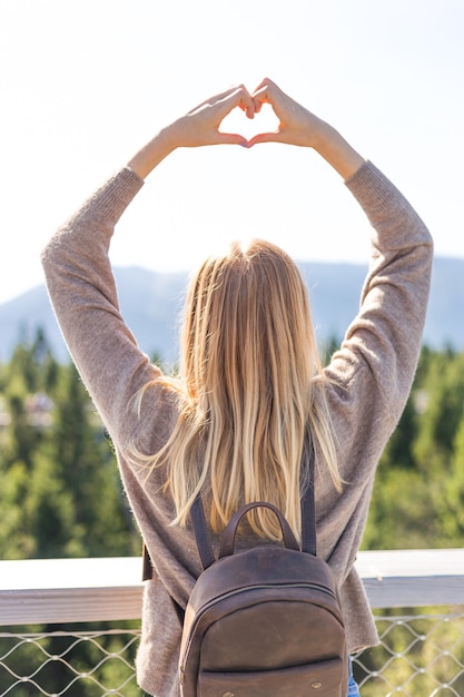 Chica haciendo una forma de corazón con paisaje de montaña de fondo.