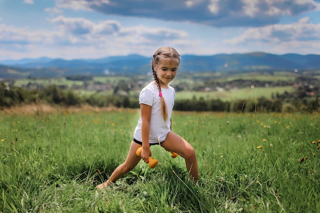 Chica haciendo sus ejercicios matutinos con mancuernas en la cima de las montañas en verano