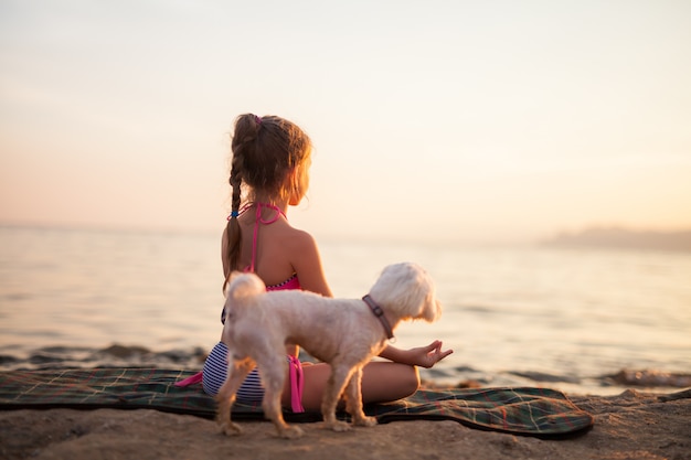 Chica haciendo yoga con su perro en la naturaleza al aire libre al amanecer