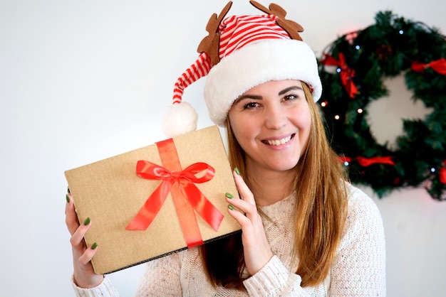 Chica hermosa feliz, mujer joven con caja de regalo de Feliz Navidad en la mano en el sombrero de Santa Claus