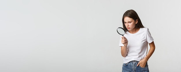 Chica hermosa inteligente de aspecto serio mirando a través de una lupa hacia abajo buscando algo
