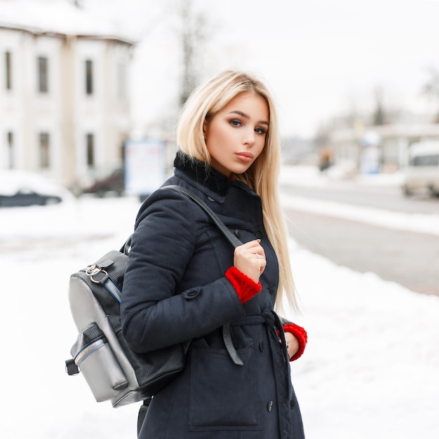 Chica hermosa joven modelo en un abrigo de invierno de moda con una bolsa en la calle