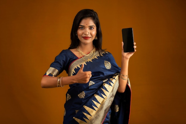 Chica hermosa joven que muestra una pantalla en blanco de teléfono inteligente o teléfono móvil o tableta