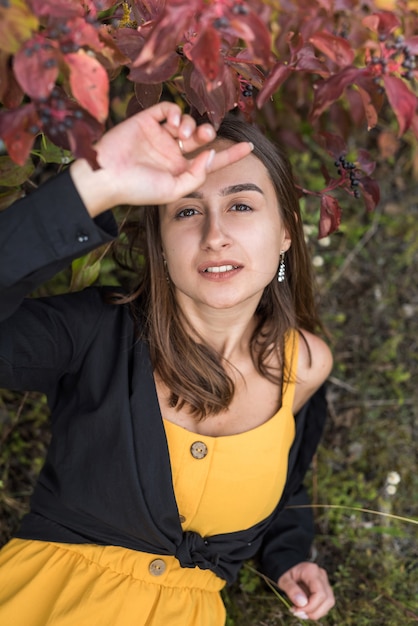 Chica hermosa y linda cerca de arbusto de follaje colorido en un parque, ambiente otoñal