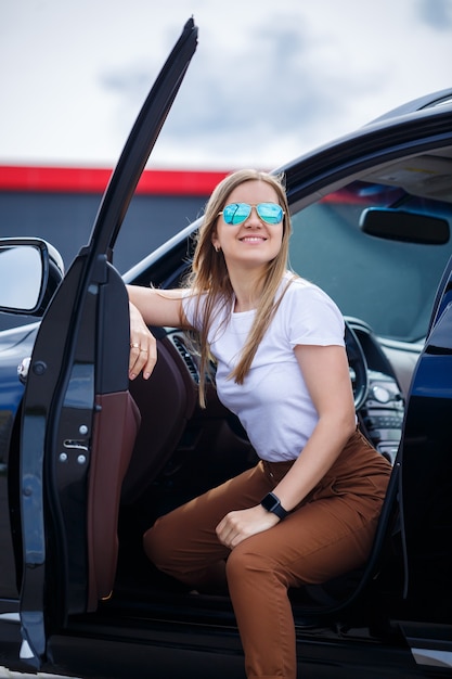 Chica hermosa de moda elegante sentada en el salón de un coche de clase ejecutiva negro. Mujer joven con una sonrisa en su rostro.