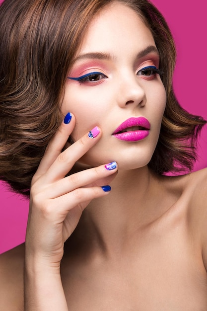 Chica hermosa modelo con maquillaje brillante y esmalte de uñas de colores Rostro de belleza Uñas cortas y coloridas Foto tomada en el estudio sobre un fondo rosa