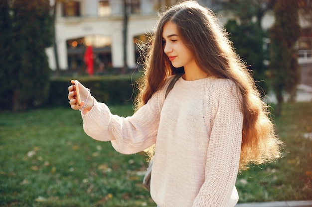 chica hermosa y de pelo largo caminando por la ciudad soleada de primavera y usando el teléfono