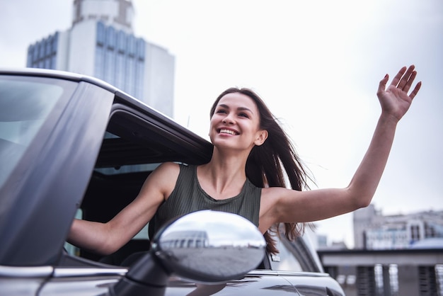 Foto una chica hermosa está saliendo por la ventana saludando y sonriendo mientras conduce un coche