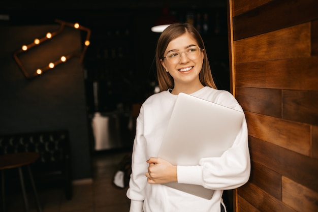 Chica con una hermosa sonrisa sostiene una computadora portátil en sus manos