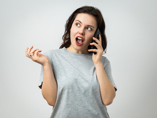 Foto una chica hermosa con un teléfono en la mano está asombrada por algo que ve lejos