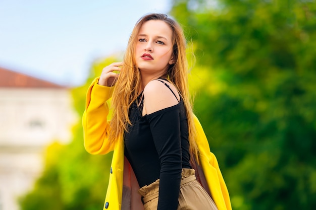 Chica con hermosas poses de maquillaje en blusa negra y abrigo amarillo