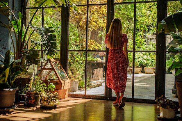 Chica en hermoso vestido rojo mirando por la ventana