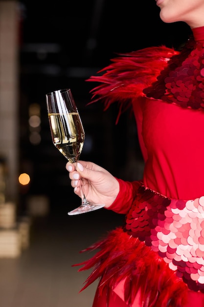 Una chica con un hermoso vestido rojo sostiene una copa de champán en sus manos.