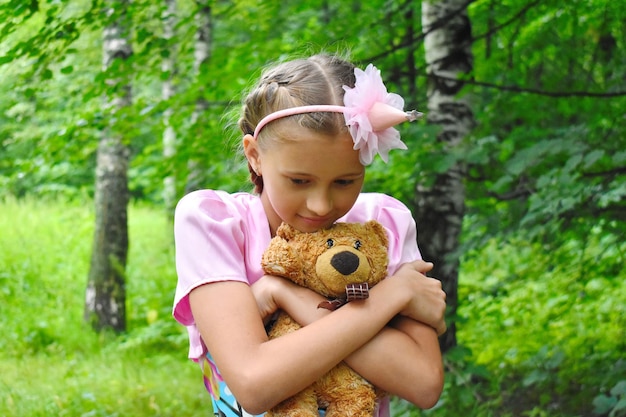 Chica con un hermoso vestido rosa con un oso de peluche. Chica, la princesa guarda un juguete en un jardín en verano.