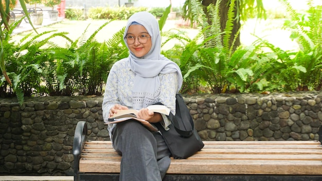 Chica hijab asiática leyendo en el jardín del campus
