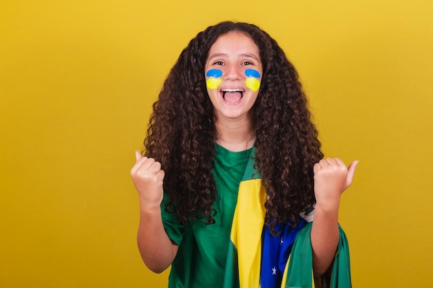 Chica hincha de fútbol caucásica brasileña celebrando con los brazos levantados