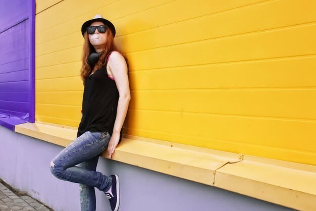 Chica hipster con auriculares en la pared