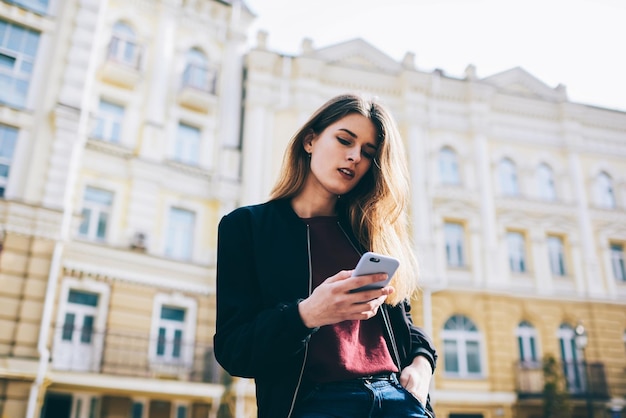 Chica hipster envía mensajes de texto y busca información sobre rutas turísticas a través de teléfonos celulares al aire libre