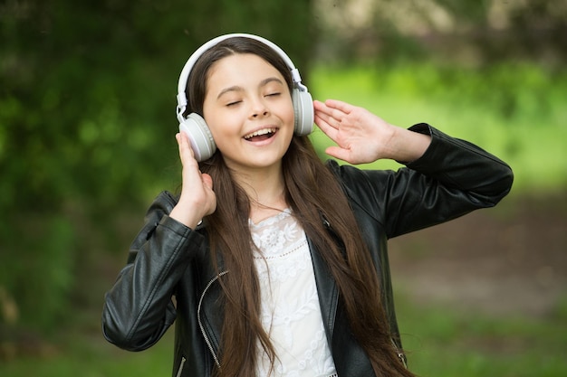 Chica hipster escuchando música auriculares modernos fondo de naturaleza cantando concepto de hobby