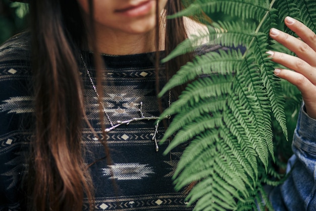 Foto chica hipster con estilo sentada en arbustos de helecho entre hojas de helecho en el primer plano del bosque de la rama de plata collar concepto ambiental espacio para texto momento atmosférico protección de la naturaleza