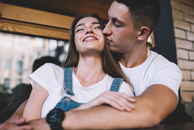 Chica hipster feliz disfrutando del tiempo junto con el cuidado de su novio abrazándose y besándose en un momento positivo