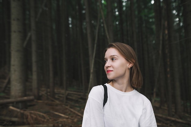 Chica hipster haciendo senderismo en el bosque de montaña posando en la cámara y sonriendo