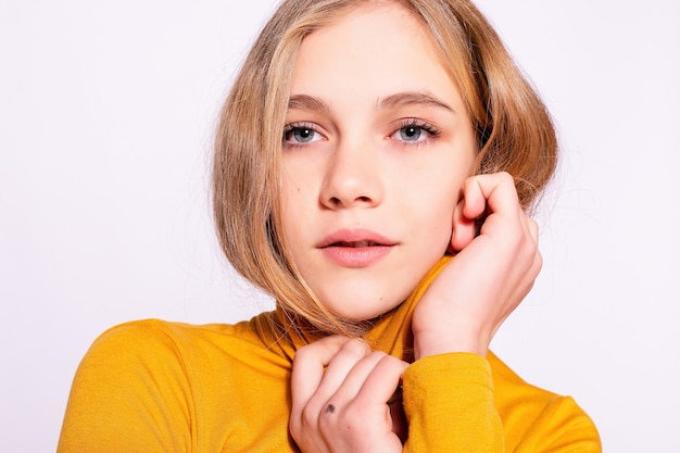 Chica hipster hermosa de moda. Foto de mujer bonita joven positiva en amarillo hasta la rodilla con fondo blanco. manos en la cara