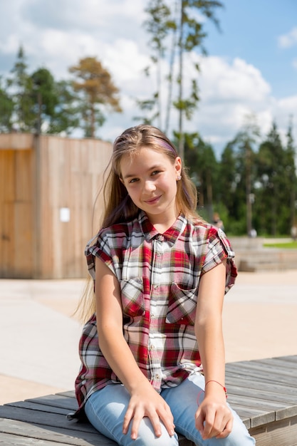 Chica hipster sonriente sentada en un banco en el parque de la ciudad