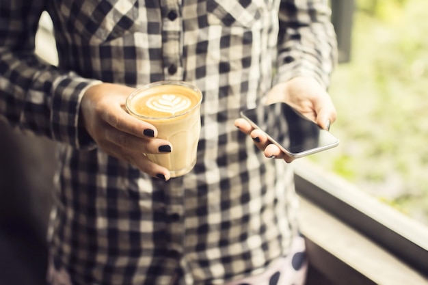 Chica hipster con taza de café y teléfono inteligente