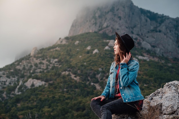 Chica hipster viajero feliz en la cima de las montañas nubladas