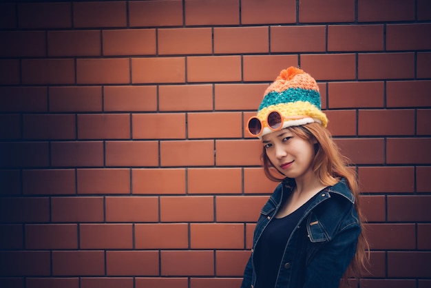 Chica de hipsters asiáticos en pared de ladrillo naranjaestilo de vida de adolescente modernoFeliz dama posando para tomar una fotogente de Tailandiagafas de sol naranjasvintagetono de películadedo medio
