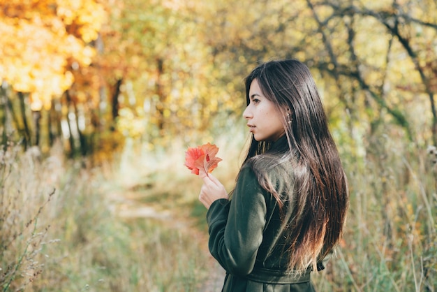 Chica con hoja roja en bosque otoñal al amanecer.