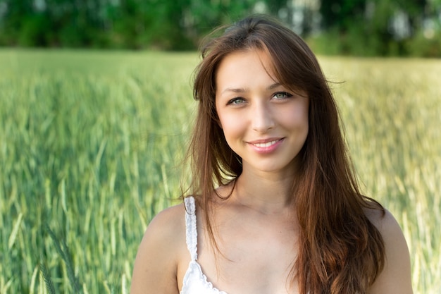 Foto chica hombros abiertos magnífico cabello oscuro sonriendo en campo de trigo verde borrosa