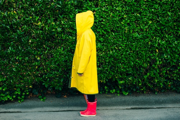 Chica en un impermeable amarillo sobre un fondo de una pared con hierba