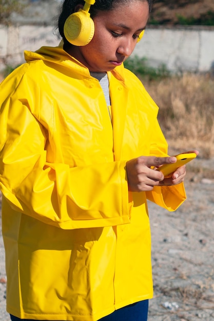 Chica en impermeable paseando al aire libre, comprobando su teléfono celular