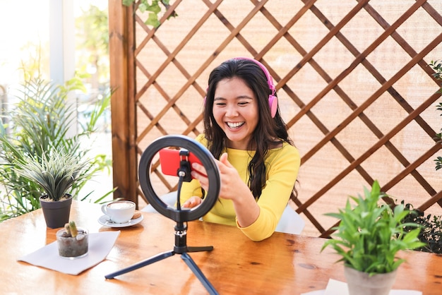 Chica influyente asiática transmitiendo en línea con cámara de teléfono inteligente al aire libre en el restaurante