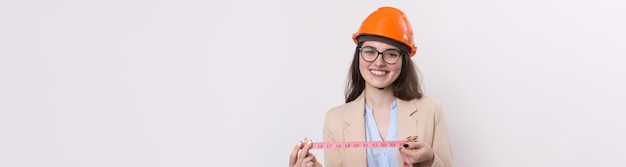 Chica ingeniera en un casco de construcción naranja con una cinta métrica en sus manos sobre un fondo blanco