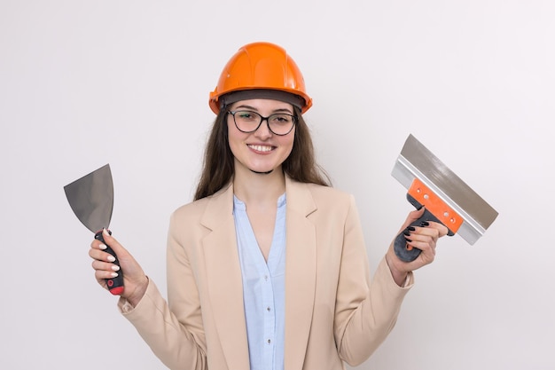 Chica ingeniera en un casco de construcción naranja con herramientas de pintura de yeso en sus manos sobre un fondo blanco