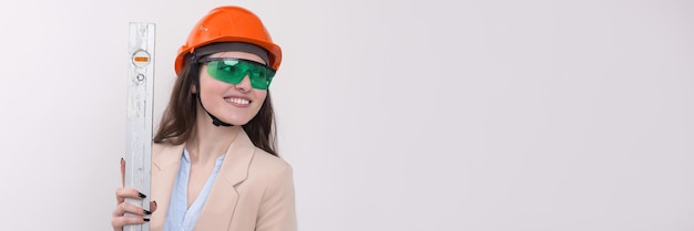 Chica ingeniera en un casco de construcción naranja con un nivel de construcción en sus manos sobre un fondo blanco