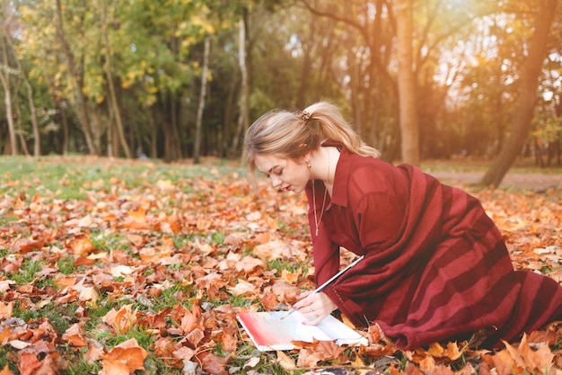 Chica se inspira para la creatividad sentada en el parque de otoño y pintando