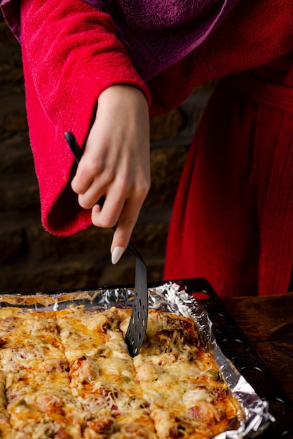 Chica irreconocible toma un pedazo de pizza casera La mano de una mujer con uñas largas sostiene una espátula de cocina