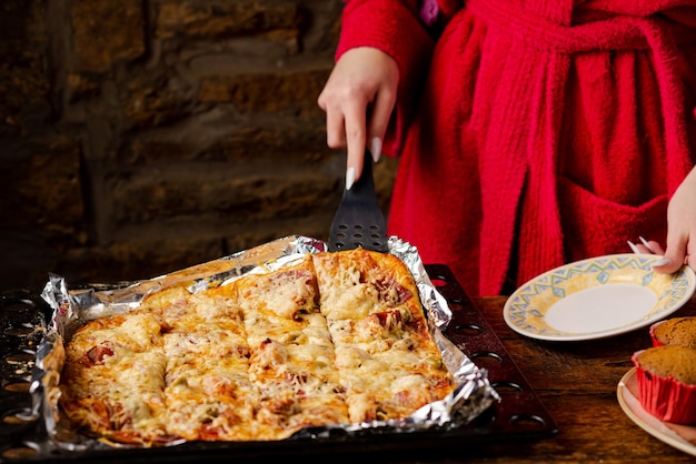 Chica irreconocible toma un pedazo de pizza casera La mano de una mujer con uñas largas sostiene una espátula de cocina