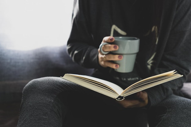 Chica irreconocible tomando un café y leyendo un libro