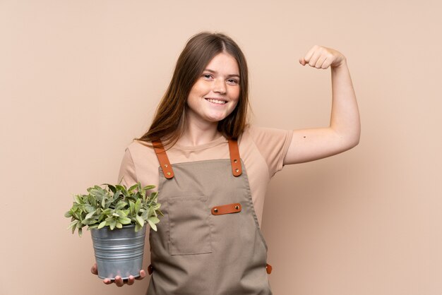 Chica jardinero adolescente sosteniendo una planta celebrando una victoria