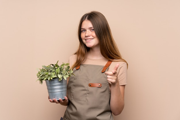 chica jardinero adolescente sosteniendo una planta te señala con el dedo