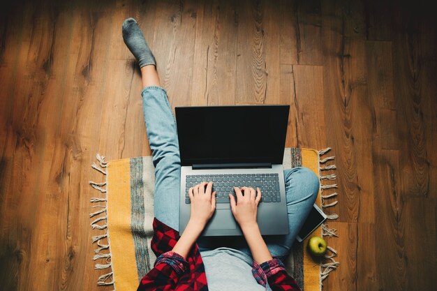 Chica en jeans con una computadora portátil. El proceso de trabajo. Se sienta en el suelo. Teléfono y manzana.